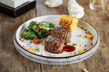 Portion of grilled fillet mignon steak with corn on wooden background