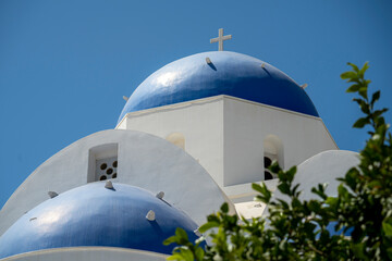 Blue and white colored Greek orthodox church, bells and cross roof, during a sunny summer day