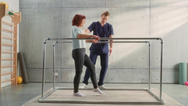 Physical Therapy Sports Center: Portrait of Strong Middle Aged Female Patient with Injury Successfully Walks Holding Parallel Bars. Physiotherapist, Rehabilitation Hospital Doctor, Medical Help.