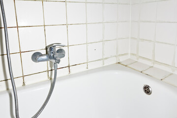 Spring cleaning concept: filthy shower armature in bath tub with black mold growing on...