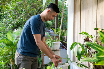 Asian young man on the terrace of his house tending his plants and succulents with some other plants.