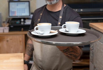 a waiter working in a coffee shop or bar holding a tray with coffees