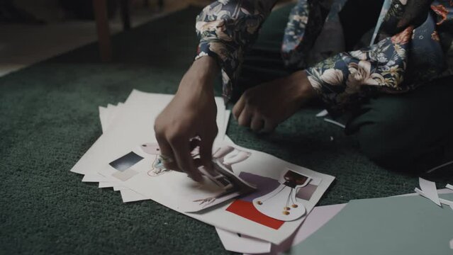 Handsome young Indian fashion designer creating inspirational trendy mood board from cut out pictures, sitting on floor in creative messy workshop