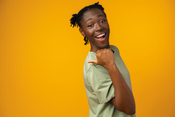 Cheerful Afro woman points to copy space in yellow studio