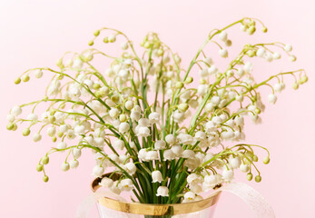 Delicate romantic bouquet of small white lilies of the valley on pink background.