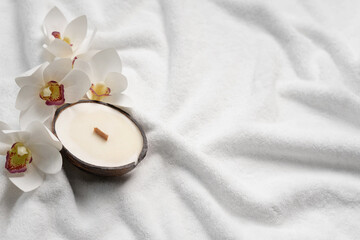 Obraz na płótnie Canvas Aroma candle in coconut shell and orchid flowers on a white terry towel. Spa mockup with copy space.