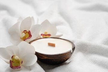 Fototapeta na wymiar Aroma candle in coconut shell and orchid flowers on a white terry towel. Spa mockup with copy space.