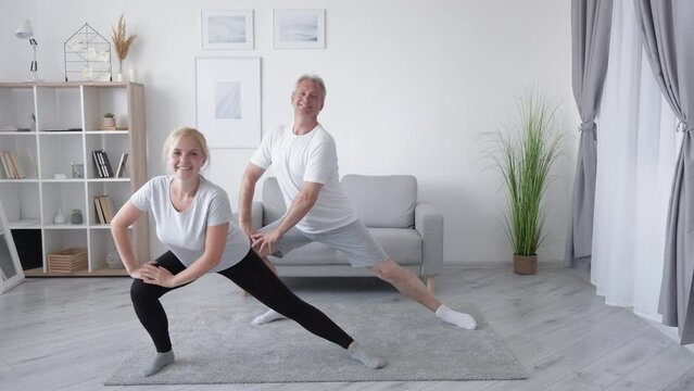 Home fitness class. Family workout. Group training. Enthusiastic smiling middle-aged father daughter doing legs strengthening lunge exercise together in light interior.
