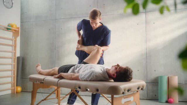 Young Male Athlete Undergoing Physiotherapy, Professional Sport Masseur Treating Light Muscle or Joint Injury. Musculoskeletal Pain Therapy and Rehabilitation Concept.