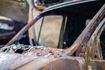 The car was completely destroyed by fire. Abandoned, burnt and rusty car by the road. Cars were on fire in the parking lot. War of Russia against Ukraine. Shrapnel and bullet holes in cars.