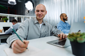 Obraz premium Young bald business man sitting at desk in office, working on computer