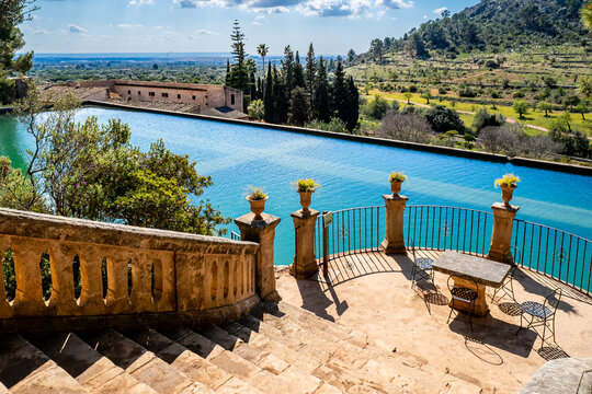 An old staircase leads down to a semicircular terrace with a stone table and four chairs that adjoins a big water reservoir, which irrigated the gardens of Raixa, a famous public Majorcan mansion.