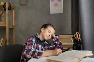 school girl is sleeping on open book while doing homework at home, tired from studying, exhausted. Distance learning, homeschooling, remote education