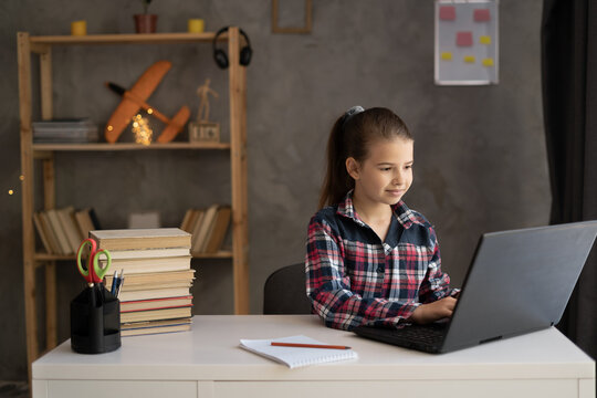 happy girl schoolgirl typing on laptop and doing homework at home. people, children, education and learning