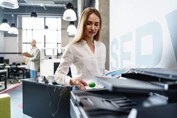 Young employee using modern printer in office