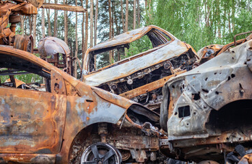 Fototapeta na wymiar A view of burnt-out cars after rocket attacks by the Russian military. War of Russia against Ukraine. Civil vehicle after the fire. Cemetery of cars in the city of Irpin. Rusty pile of metal.