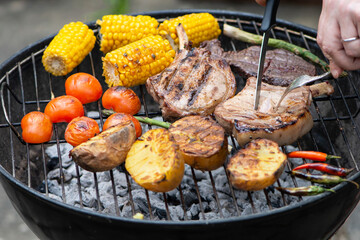 baked appetizing pork steak and potatoes with vegetables on the barbecue grill