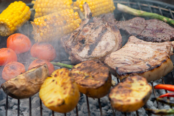 baked appetizing pork steak and potatoes with vegetables on the barbecue grill