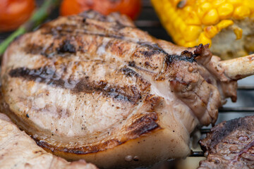 baked appetizing pork steak and potatoes with vegetables on the barbecue grill