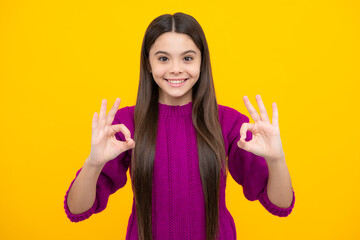 Beautiful child girl making ok sign on yellow background. Portrait of smiling kid show confident hands symbol. Teenager girl showing okey gesture.