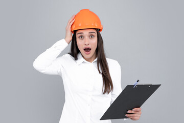 Surprised shocked excited business woman with clipboard, portrait on gray. Young woman in helmet hold laptop computer on gray background. Architect businesswoman.