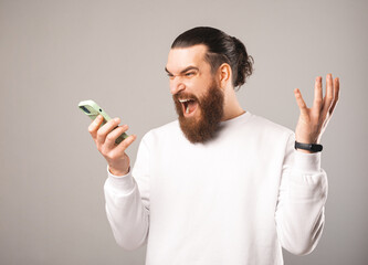 Photo of young angry man with beard screaming at smartphone talking woth someone.