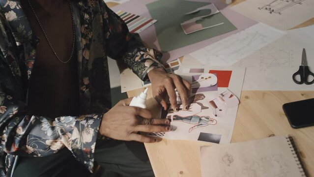 Indian fashion designer using liquid glue while making inspirational mood board, sitting at wooden worktable in creative messy workshop