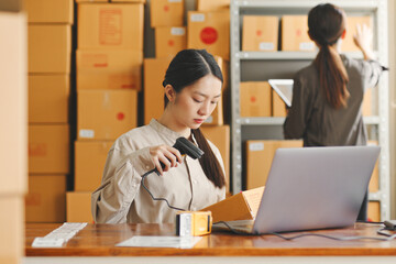 Asian woman working at online store warehouse, using barcode reader check on customer parcel box,...
