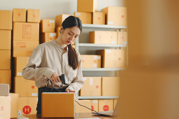 Asian woman working at online store warehouse, using barcode reader check on customer parcel box,...