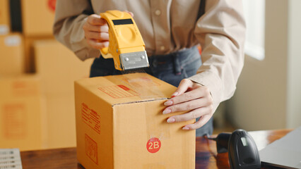 Asian woman working at online store warehouse packing product to parcel cardboard boxes, online...