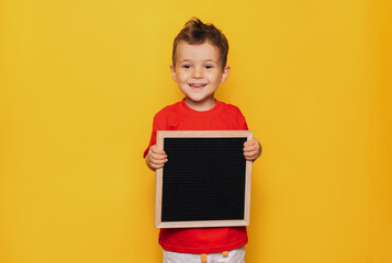 Studio portrait of a Caucasian boy with a black letter board in his hands on a bright yellow...