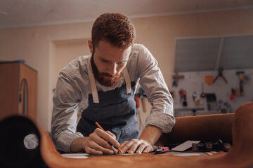 Man tailor or cobbler measuring and cutting brown leather on workplace handmade