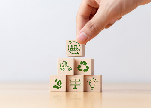 Carbon neutral and net zero concept. Balance between the amount of greenhouse gas produced and the amount removed from the atmosphere. Hand puts wooden cubes with Net Zero icon on table.