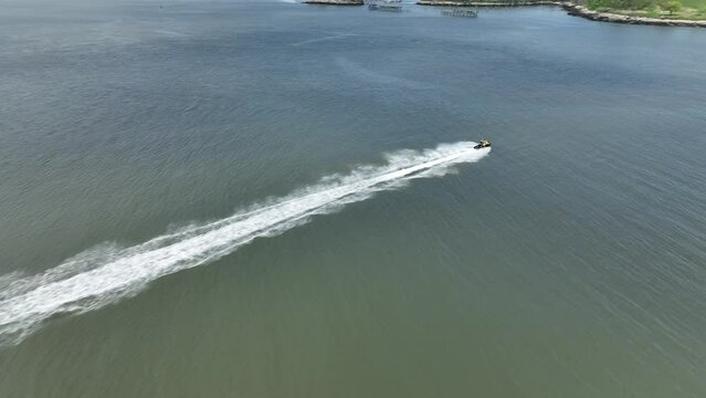 An aerial view over Gravesend Bay in Brooklyn, NY as a jet ski rider enjoys the beautiful day. The drone camera tilted down, trucks right, pan right then dolly in to follow the jet skier racing out.