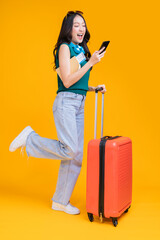 ready to travel ,asian smiling cheerful woman hand using smartphone credit card pull luggage bag prepare to new abroad journey travel studio shot on yellow background