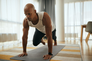 Fototapeta premium Young African American athletic man in plank pose doing running abs exercise during home workout.