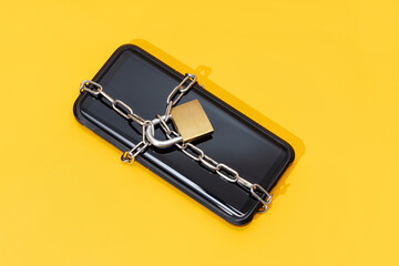 Phone security concept. Smartphone locked with chain and padlock on yellow background. Mobile...