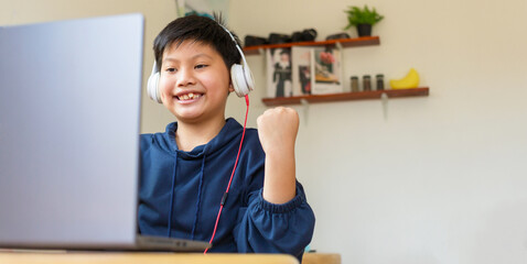 An Asian boy wearing headphones raises his hands in joy after completing an online study.