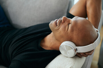Relaxed African American man enjoys in music over headphones at home.
