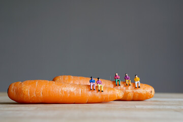 Miniature figurine character: people sitting on carrots, concept of fresh organic vegetables for good health in the market, selected focus