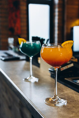 two glasses with colored cocktails on the bar counter