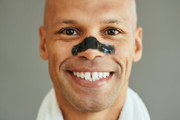 Close up of happy African American man using cleansing nose strips for blackhead treatment.