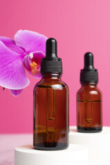 Beauty collagen face oil in a glass dropper bottles on podium with orchid flowers. Trendy shoot of cosmetics packaging. Essential oil with natural ingredients.