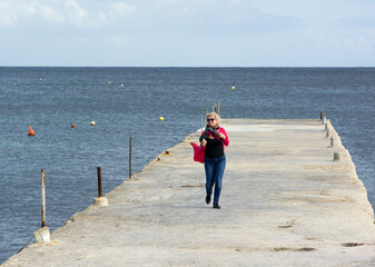 Alone blond woman enjoying sunny winter day in Malta,St Thomas bay. Windy sunny day in Marsaskala St Thomas bay, Malta.Woman enjoying nature in nice view to the sea, Malta.