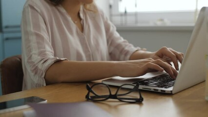 In this footage you can see young professional caucasian female working with laptop computer in home office or small agency studio. Her hands typing on keyboard while writing a text or letter.