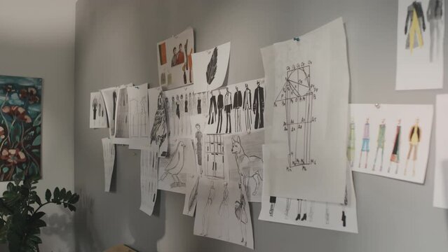 Male Indian fashion designer attaching sketch to wall with other sketches and inspirational ideas in creative workshop