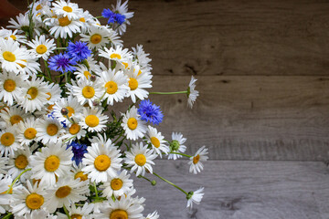Obraz premium Midsummer bouquet of summer flowers white daisies and blue cornflowers in the vase on wooden background with copy space. Top view