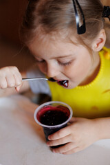 Portrait of pretty 4-year-old little baby girl eating jelly sweets at home at her child table....