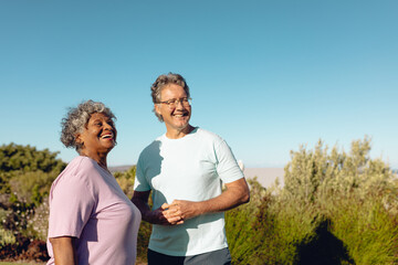 Multiracial happy senior friends standing against plants against clear blue sky during sunny day