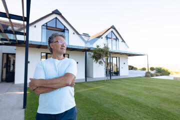 Fototapeta premium Thoughtful caucasian senior man with arms crossed standing against nursing home in yard, copy space